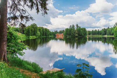 Sahilden manzaralı, gölde ahşap kürkler ve eski Arch Köprüsü. Yaz, mavi gökyüzü, bulutlar, suda yansıma