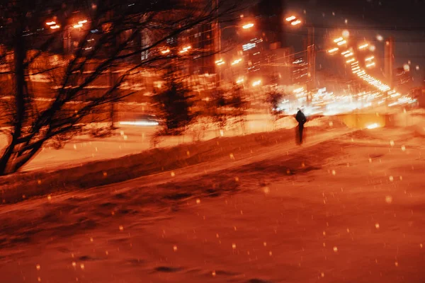 Tarde en la noche. Invierno, ciudad iluminada calle, nieve, silueta joven. Fondo borroso. Concepto meteorológico — Foto de Stock