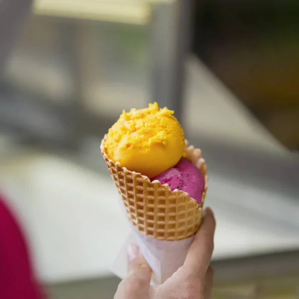 Two balls of fruit ice cream in waffle cone in female hand. Selective focus. Real scene — Stock Photo, Image