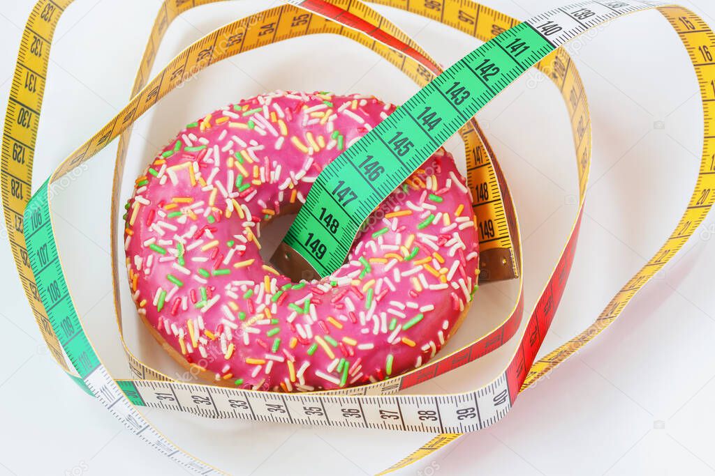 Glazed donut and tape measure close-up. Concept of healthy food, diet, overweight