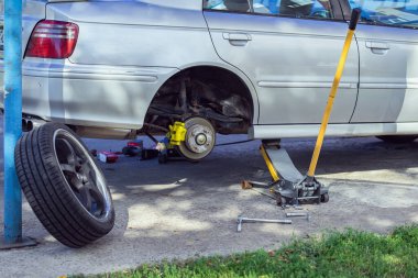 Car without rear wheel lifted on hydraulic jack during repair in outdoor workshop. Concept of car repair, wheel replacement, maintenance service and mechanical work