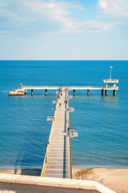 Long pier stretching into calm blue sea in Burgas, Bulgaria, with people walking under soft sunlight and open sky. Concept of Burgas seafront, Black Sea travel, peaceful coastal escape