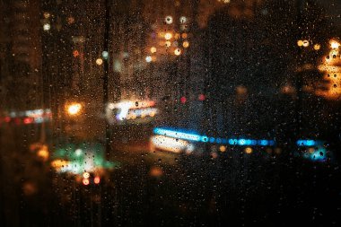 Bulanık şehir ışıkları gece boyunca parlarken yağmur damlaları yavaşça pencereden süzülüyor. Yalnızlık kavramı, duygusal sessizlik, yağmurlu yalnızlıkta görünmeyen varlık.