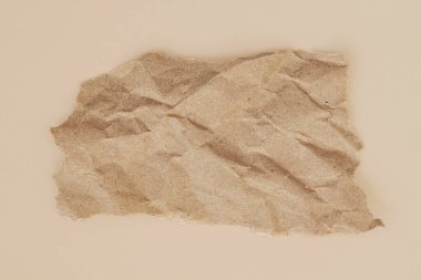 Kahverengi desenli yırtık kağıt, düz bej bir yüzey, ham kenarlar ve düz olmayan kağıt formunda yatar. Yüzeyin doğal dokusu, boşluğu kopyala