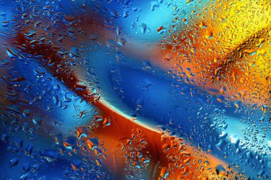 Su damlacıkları cam yüzeyde soyut mavi, turuncu ve sarı renklerin karışımı. Sıvı hareket, sanatsal doku, canlı modern renk kombinasyonları. Soyut parlak modern arkaplan