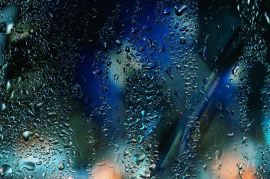 Arka planda karamsar neon ışıkları olan camlara su damlaları çarpıcı soyut desenler ve moda renkler yaratır. Melankoli kavramı, yağmur, şehir havası, sinematik zemin