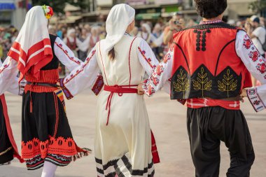 Kültür festivali sırasında Bulgar halk kostümlü insanlar el ele tutuşup dans ediyorlar. Geleneksel Bulgar halk kıyafetleri giyen katılımcılar, kent merkezinde halka açık kültür festivali daireler çizerek dans ediyorlar