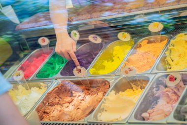 Büfede dondurma sergisi. Camın arkasında renkli dondurma aromaları ve dondurma seçimini gösteren el işaretleri var. Dondurma seçimi, tatlı seçimi, dondurmacıda tüketici seçimi