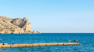 Sudak, Kırım - 20 Eylül 2020: Alchak kayasının karşısındaki taştan bir rıhtımdaki insanlar