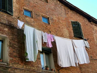 Siena, İtalya 'da eski bir evin tuğla duvarının arkasındaki ipte çarşaf var.