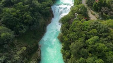 El Naranjo, San Luis Potosi 'deki El Meco Şelalesinin güzelliğini görün. Tropikal bir ortamda yeşil ağaçların ve tepelerin ortasındaki şelaleye tanık olun..