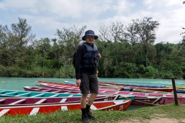 Huasteca Potosina 'daki Cascada del Meco nehrinin kenarındaki renkli teknelerin yanında bir kişi duruyor. Bölge tropikal bitkiler ve ağaçlarla dolu. Sahne canlı ve canlı..