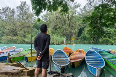 Huasteca Potosina 'daki Cascada del Meco nehrinin kenarındaki renkli teknelerin yanında bir kişi duruyor. Bölge tropikal bitkiler ve ağaçlarla dolu. Sahne canlı ve canlı..