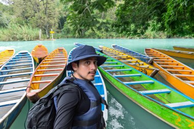 Huasteca Potosina 'daki Cascada del Meco nehrinin kenarındaki renkli teknelerin yanında bir kişi duruyor. Bölge tropikal bitkiler ve ağaçlarla dolu. Sahne canlı ve canlı..