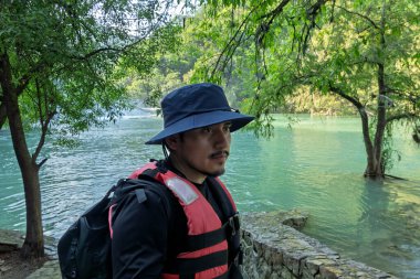 San Luis Potosi, Huasteca Potosina 'daki Cascada de Micos' da bir kişi suyun yanında duruyor. Sahne, arka planda birden fazla şelale bulunan tropikal bitki örtüsü ve berrak suyu gösteriyor..