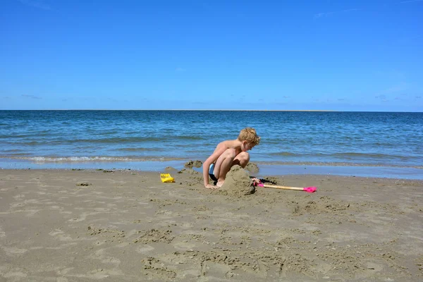 Blondyn Kąpielówkami Buduje Zamek Piasku Plaży Przed Morzem Niebieskim Niebem — Zdjęcie stockowe