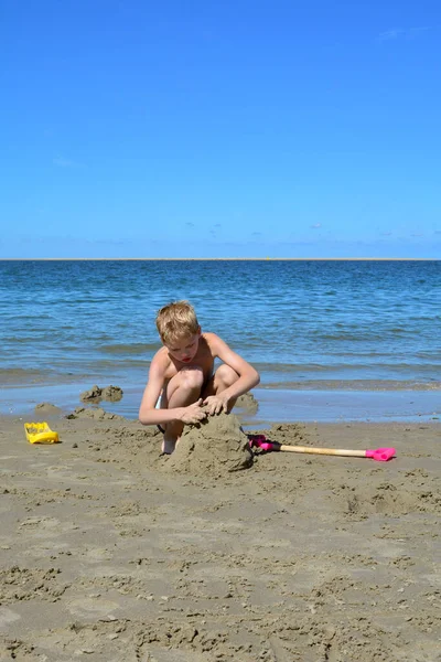Jeden Blondyn Kąpielówkami Buduje Zamek Piasku Plaży Przed Morzem Błękitnym — Zdjęcie stockowe