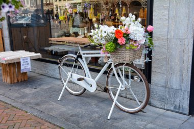 Tipik Hollanda - Hollanda 'nın Zieriksee kentindeki bir dükkanın önünde elinde çiçek sepeti olan beyaz bisiklet duruyor.