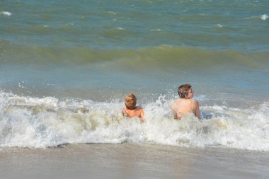 İki çocuk, Hollanda 'nın Kuzey Denizi kıyısındaki dalgaların ortasında kumlu sahilde neşe içinde oturuyor.