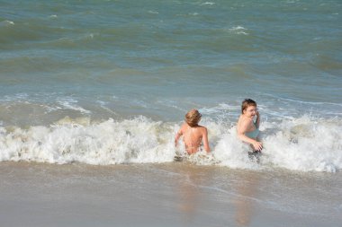 İki çocuk, Hollanda 'nın Kuzey Denizi kıyısındaki dalgaların ortasında kumlu sahilde neşe içinde oturuyor.