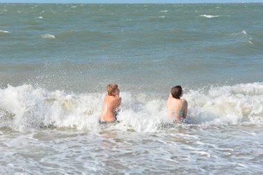 İki çocuk, Hollanda 'nın Kuzey Denizi kıyısındaki dalgaların ortasında kumlu sahilde neşe içinde oturuyor.