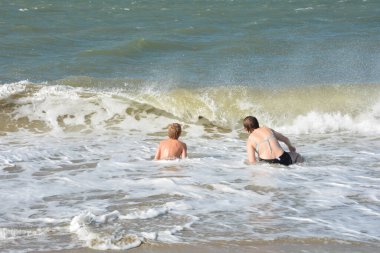 İki çocuk, Hollanda 'nın Kuzey Denizi kıyısındaki dalgaların ortasında kumlu sahilde neşe içinde oturuyor.