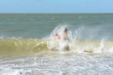 İki çocuk, Hollanda 'nın Kuzey Denizi kıyısındaki bir su sıçrayan dalganın ortasında mutlu bir şekilde otururlar.