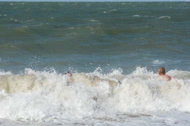 İki çocuk, Hollanda 'nın Kuzey Denizi kıyısındaki bir su sıçrayan dalganın ortasında mutlu bir şekilde otururlar.
