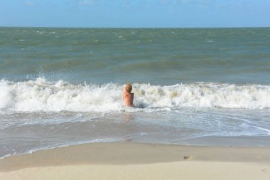 Bir çocuk, Hollanda 'nın Kuzey Denizi kıyısındaki kumlu sahilde dalgalar içinde suda oturur.