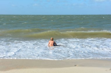 Bir çocuk, Hollanda 'nın Kuzey Denizi kıyısındaki kumlu sahilde dalgalar içinde suda oturur.