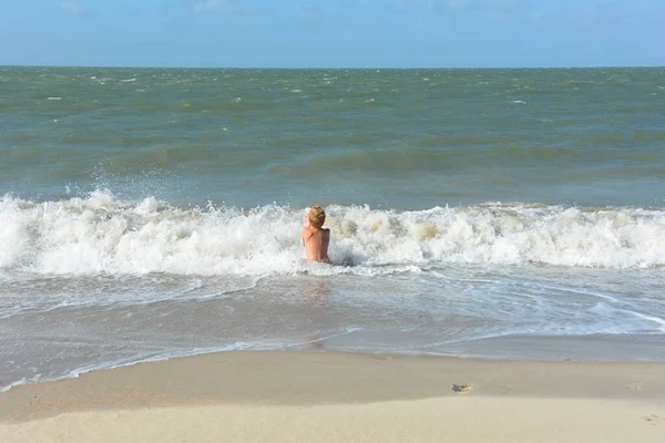 Bir çocuk, Hollanda 'nın Kuzey Denizi kıyısındaki kumlu sahilde dalgalar içinde suda oturur.