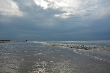 Kuzey Denizi kıyısında bulutlu gökyüzü olan kumlu bir sahilde akşam yürüyüşü