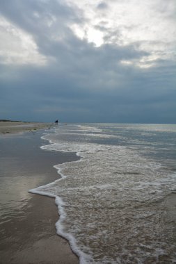 Kuzey Denizi kıyısında bulutlu gökyüzü olan kumlu bir sahilde akşam yürüyüşü