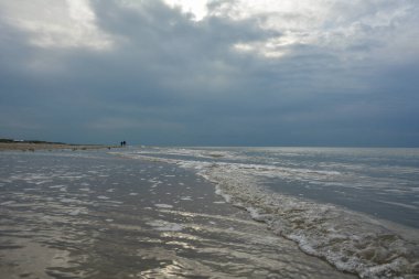 Kuzey Denizi kıyısında bulutlu gökyüzü olan kumlu bir sahilde akşam yürüyüşü