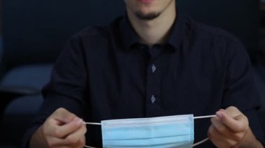 Genç doktor, bizi ve seni korumak için nasıl cerrahi maske takılacağını gösteriyor. Coronavirus dünyayı değiştiriyor. Ağızlığın yerleştirilmesi ve işe hazır olmak, iş. Video çekimi Full HD 60 fps.