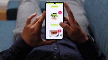 Genç bir adam online bir mağazada öğle yemeği ya da akşam yemeği için ne alacağını seçer. İnternetten al. Alışverişin geleceği. Akıllı telefonundan alışveriş yapıyorsun. Video çekimi Full HD 60 fps.