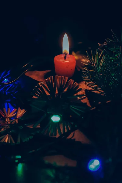 黑色背景上的深色照片配上各种彩灯 为即将到来的圣诞营造出一种美妙的精神 在后面是一根带有火焰的红色蜡烛 — 图库照片