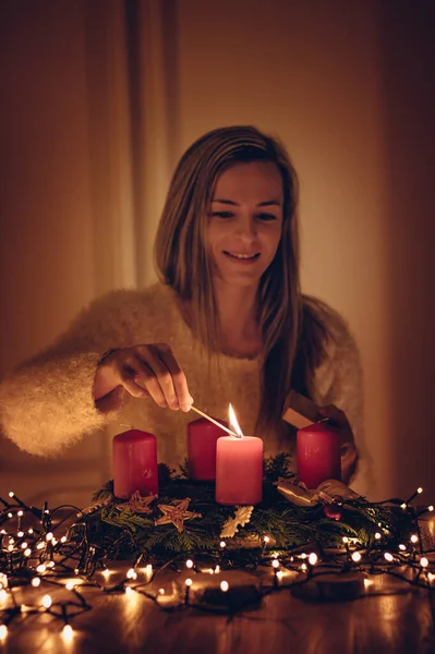 Saçları parlak genç bir kadın, bir çelengin ilk mumunu yakıyor. Noel yaklaşırken dudağından gülümseyen genç ve güzel bir kadın. Aile ve Avrupa ülkelerinin gelenekleri.