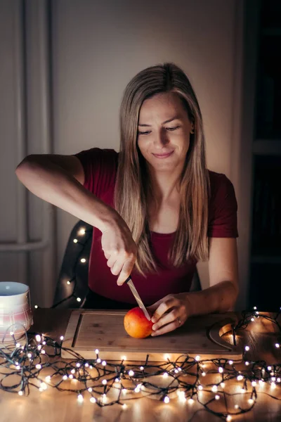 young woman of 25, with hair highlights and a red T-shirt, holds a knife and slices a red apple on a wooden plank. Faith and superstition in this custom. Merry Christmas. Snack prep.