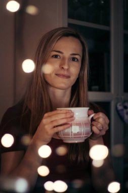 Avrupalı etnik kökenli orta yaşlı bir kadın pencereden dışarı bakıyor ve yemeğinin tadını çıkarıyor. Hayatını düşünüyor ve işten sonra dinleniyor. Kırmızı tişörtlü bir kızdan büyüleyici bir gülümseme..