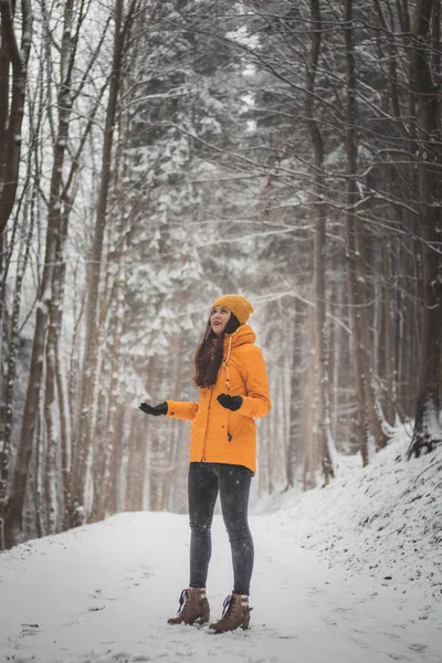 Girl of European descent and aged 20-24 rejoices in the falling snow. A woman stands in the middle of a snowy road in a yellow bold jacket and yellow hats. A real smile.