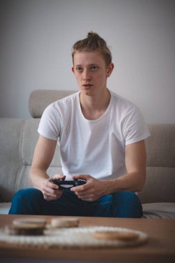 20-29 yaşlarında, sarı saçlı bir adamın odaklanmış ifadesi. Oyuncu oturma odasındaki kanepede oturur ve oyun konsolunda oynar. Bugünün e-sporcularının dünyası. Karantinada can sıkıntısı.