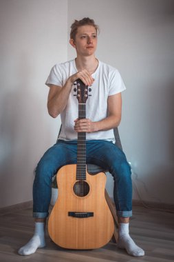 Sarı saçlı gülümseyen çocuk alçak bir taburede oturur ve önünde gitar adı verilen enstrümantal bir enstrüman tutar. 20-29 yaşlarında hayallerini gerçekleştiren bir adamın ikili portresi..