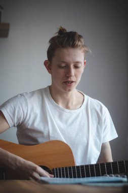 Beyaz bir duvara yaslanan, en sevdiği enstrümanı tutan ve uzaya bakan umut verici yeni bir şarkıcının ikili portresi. Bir folk şarkıcısının portresi. Sabah ışığı.