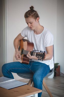 Beyaz tişörtlü, kot pantolonlu, ışıklı bir odanın ortasında oturmuş akustik gitar çalan genç bir şarkıcının gerçek gülümsemesi. Sarı saçlı ve çilli bir adam doğru akorlar için sözlüğe bakar.