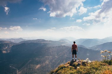 Vahşi Avusturya doğasında enerji yükleme. Kep ve kırmızı elastik hileyle daha hafif figürlü sporcu kayanın kenarında duruyor ve rahatlama ve özgürlük hissinden hoşlanıyor. Otscher Dağı Fethediliyor.