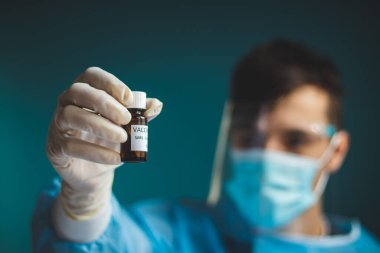 Koruyucu kalkan, duvak ve steril eldivenli doktor Coronavirus salgınına karşı tek bir silah taşıyor. Bir bilim adamı bir Covid-19 'a karşı ampul tutuyor ve kamerayı işaret ediyor..