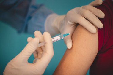 Steril koruyucu kıyafetli bir doktor kafasında bir kalkanla gelen bir hasta için Covid-19 aşısı olan bir şırınga hazırlıyor. Sağlık çalışanı. Bir salgınla savaşmak