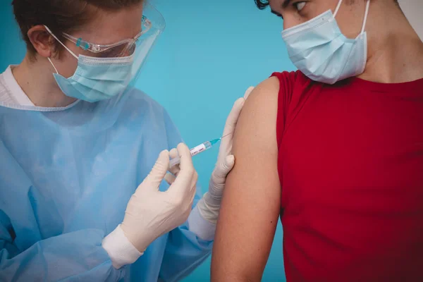 Steril elbiseli doktor genç bir adama iğne yapıyor. Covid-19 'a karşı geliştirilmiş bir aşının detayları. Dünya çapında bir sorun. Bir tutam umut. Aşı Merkezi.