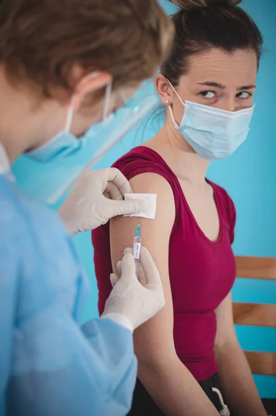 Steril ve koruyucu giysili bir doktor endişeli bir ifadeyle genç bir kadının omzuna kovid 19 aşısı enjekte ediyor. Aşı zamanı. Genel salgın.